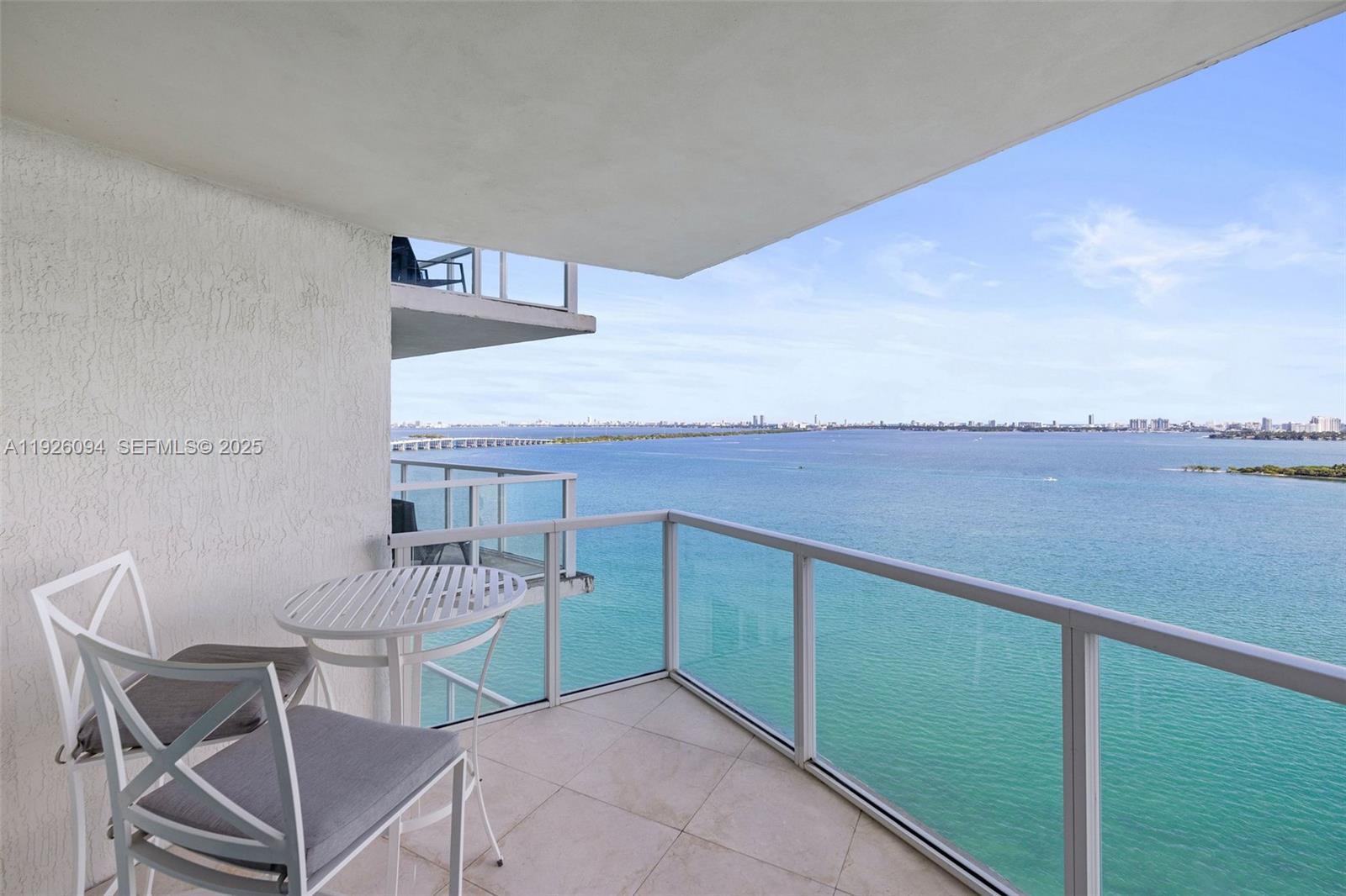 A balcony with a small table and chairs overlooks a wide bay and city skyline — 665 NE 25th St # 1801, Miami FL 33137, MIAMI, FL