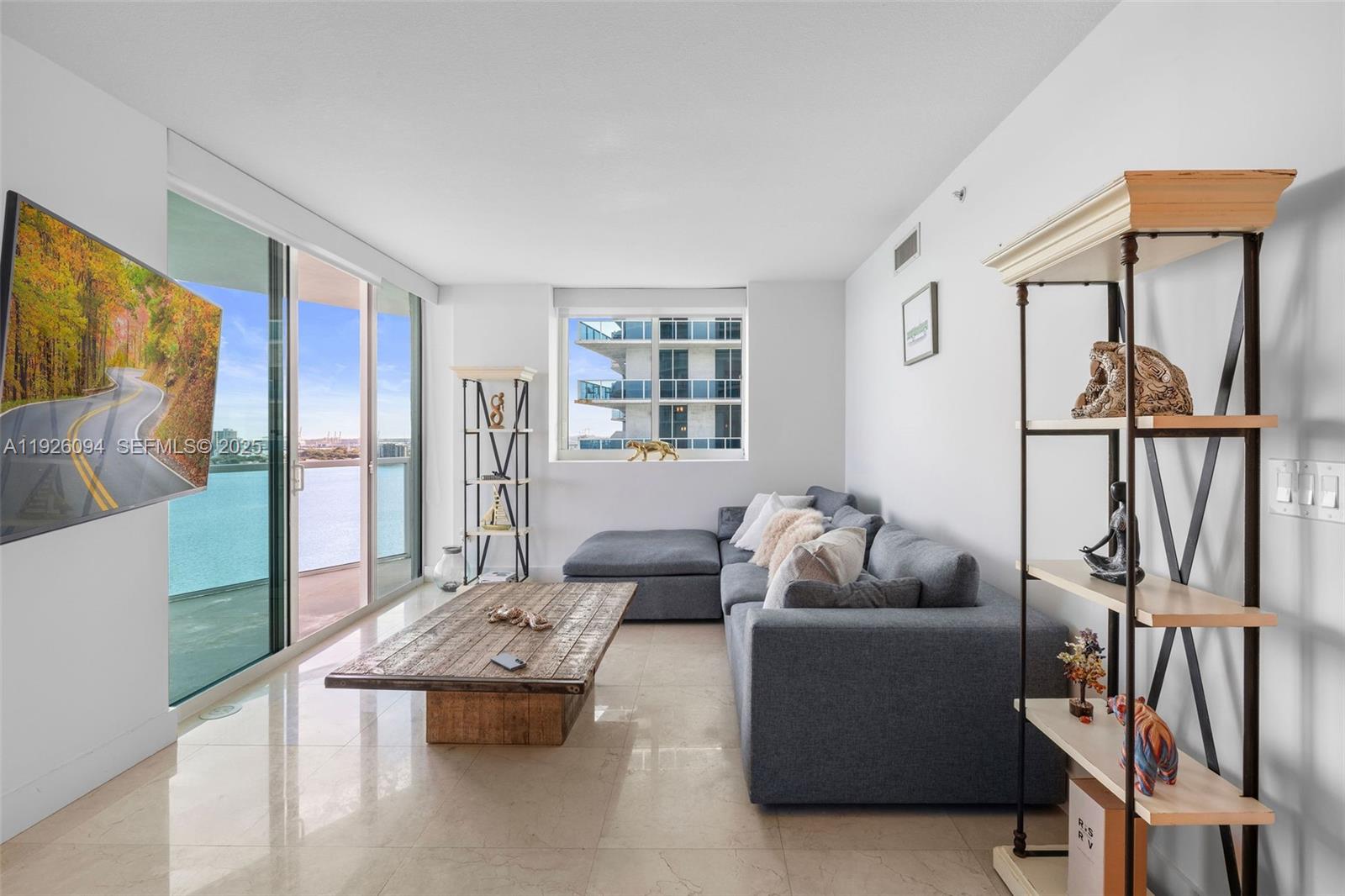 A living room features a gray sectional sofa, a wooden coffee table, and a balcony view — 665 NE 25th St # 1801, Miami FL 33137, MIAMI, FL