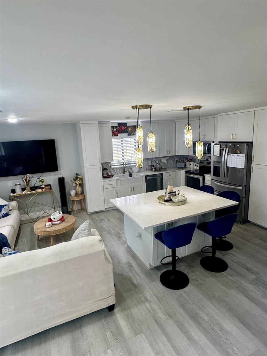 An open-concept kitchen and living area features white cabinetry, a central island, and blue stools — 4631 Cherry Road, West Palm Beach FL 33417, WEST PALM BEACH, FL
