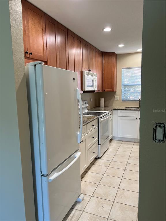 A kitchen features wood upper cabinets, white lower cabinets, a white refrigerator, and tile flooring — 2200 S PALMETTO AVENUE UNIT D030, DAYTONA BEACH, FL