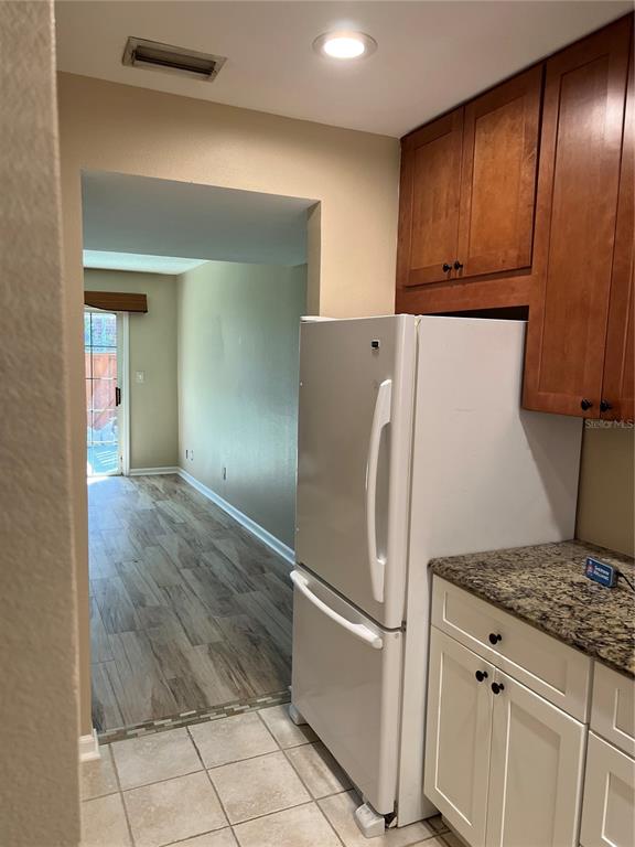A kitchen with a white refrigerator and wood cabinets leads to a room with wood-look flooring — 2200 S PALMETTO AVENUE UNIT D030, DAYTONA BEACH, FL