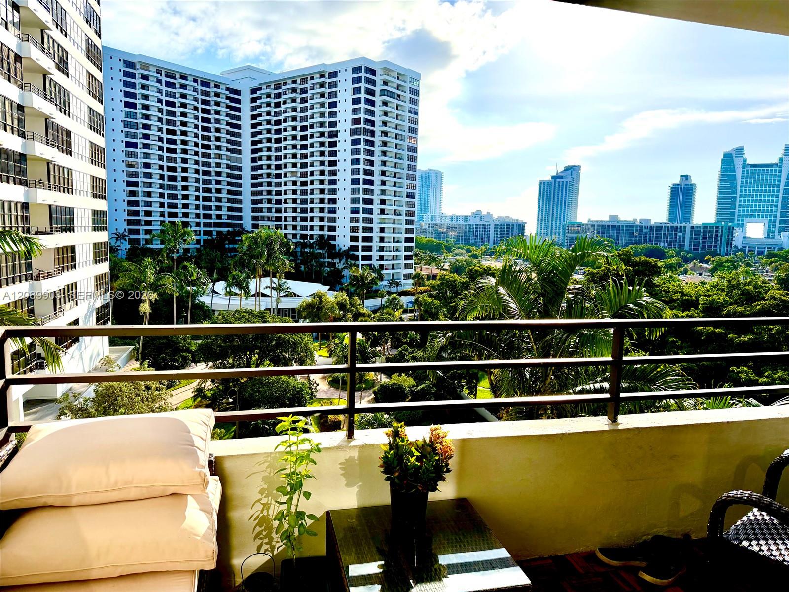 A balcony with patio furniture overlooks a lush courtyard and surrounding high-rise apartment buildings — 500 Three Islands Blvd # 421, Hallandale Beach FL 33009, HALLANDALE BEACH, FL