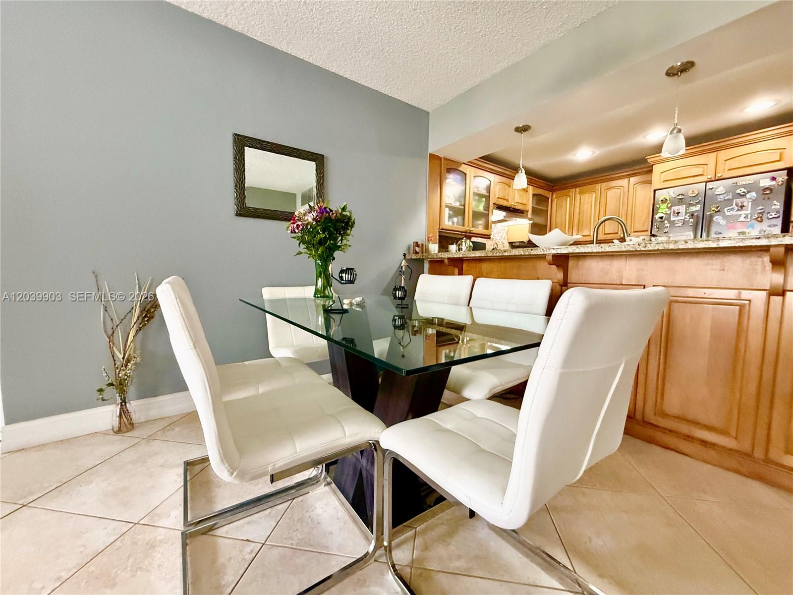 A dining area features a glass-top table, white chairs, and a view into the kitchen — 500 Three Islands Blvd # 421, Hallandale Beach FL 33009, HALLANDALE BEACH, FL