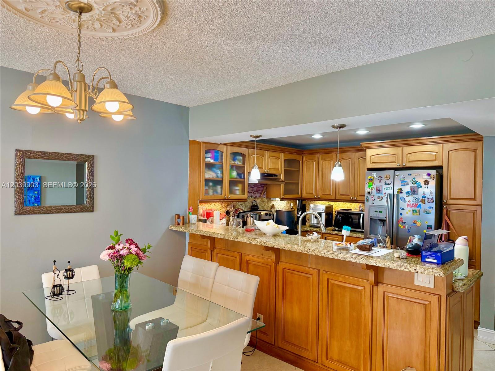 A dining area with a glass table sits adjacent to a kitchen with wooden cabinets — 500 Three Islands Blvd # 421, Hallandale Beach FL 33009, HALLANDALE BEACH, FL