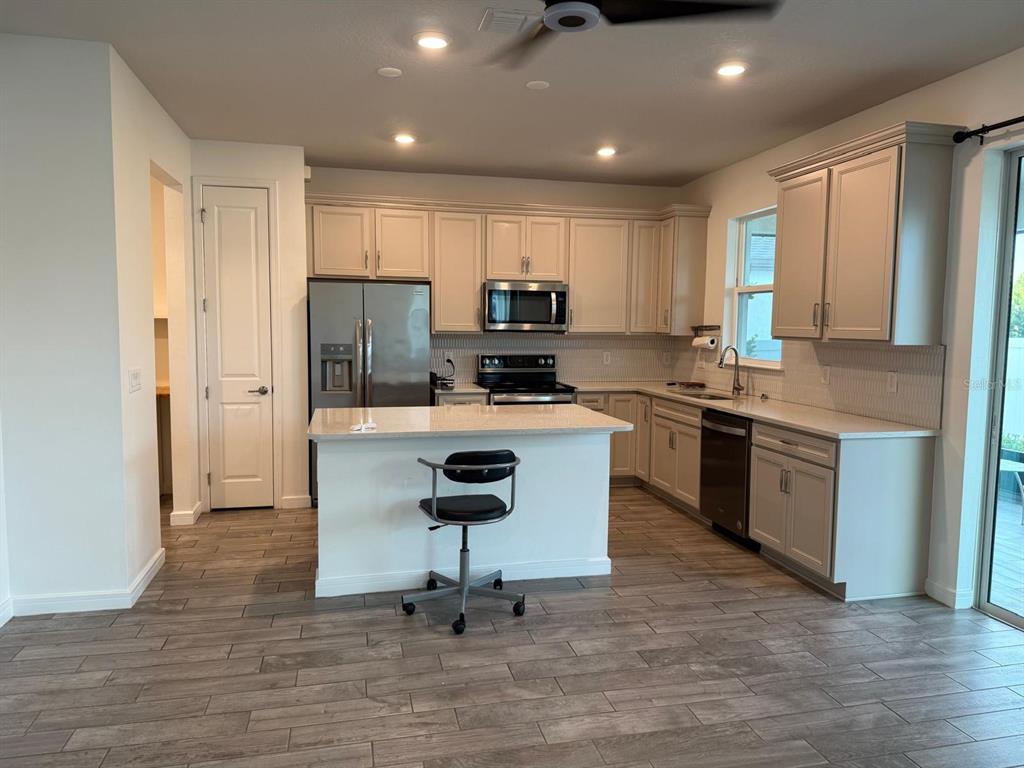 A kitchen features light-colored cabinetry, stainless steel appliances, a center island, and wood-look tile flooring — 772 PARSONS MOORING COURT, SEFFNER, FL