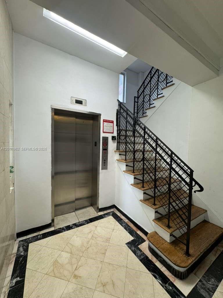 An indoor stairwell features a metal railing, a stainless steel elevator, and tiled flooring — 3700 Collins Ave # 309, Miami Beach FL 33140, MIAMI BEACH, FL