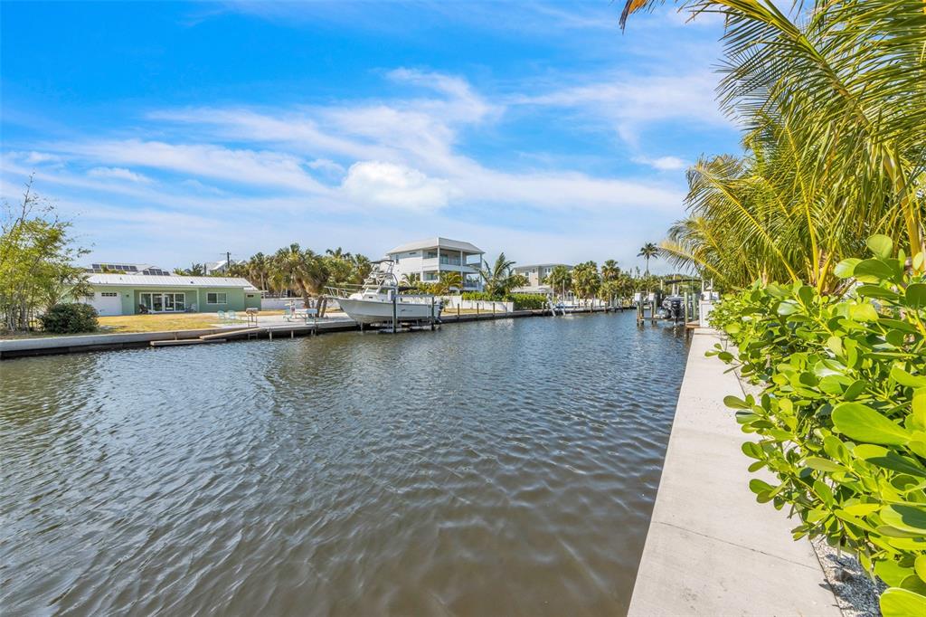 A canal view showing a boat docked at a seawall near waterfront houses and palm trees — 224 CHILSON AVENUE, ANNA MARIA, FL