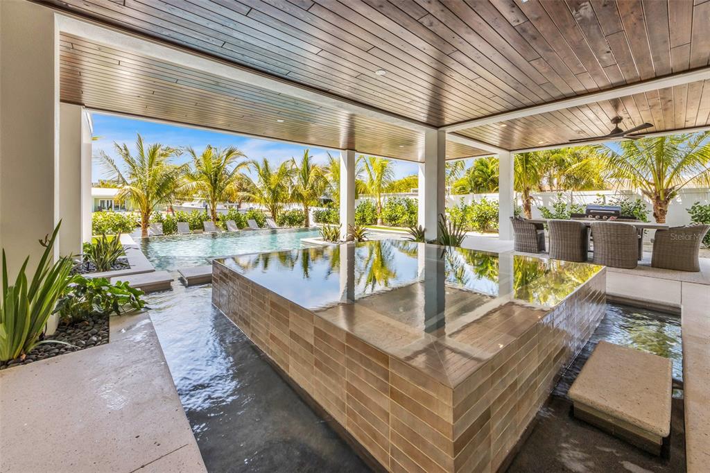 A covered patio features a raised tiled spa surrounded by a shallow pool and landscaping — 224 CHILSON AVENUE, ANNA MARIA, FL