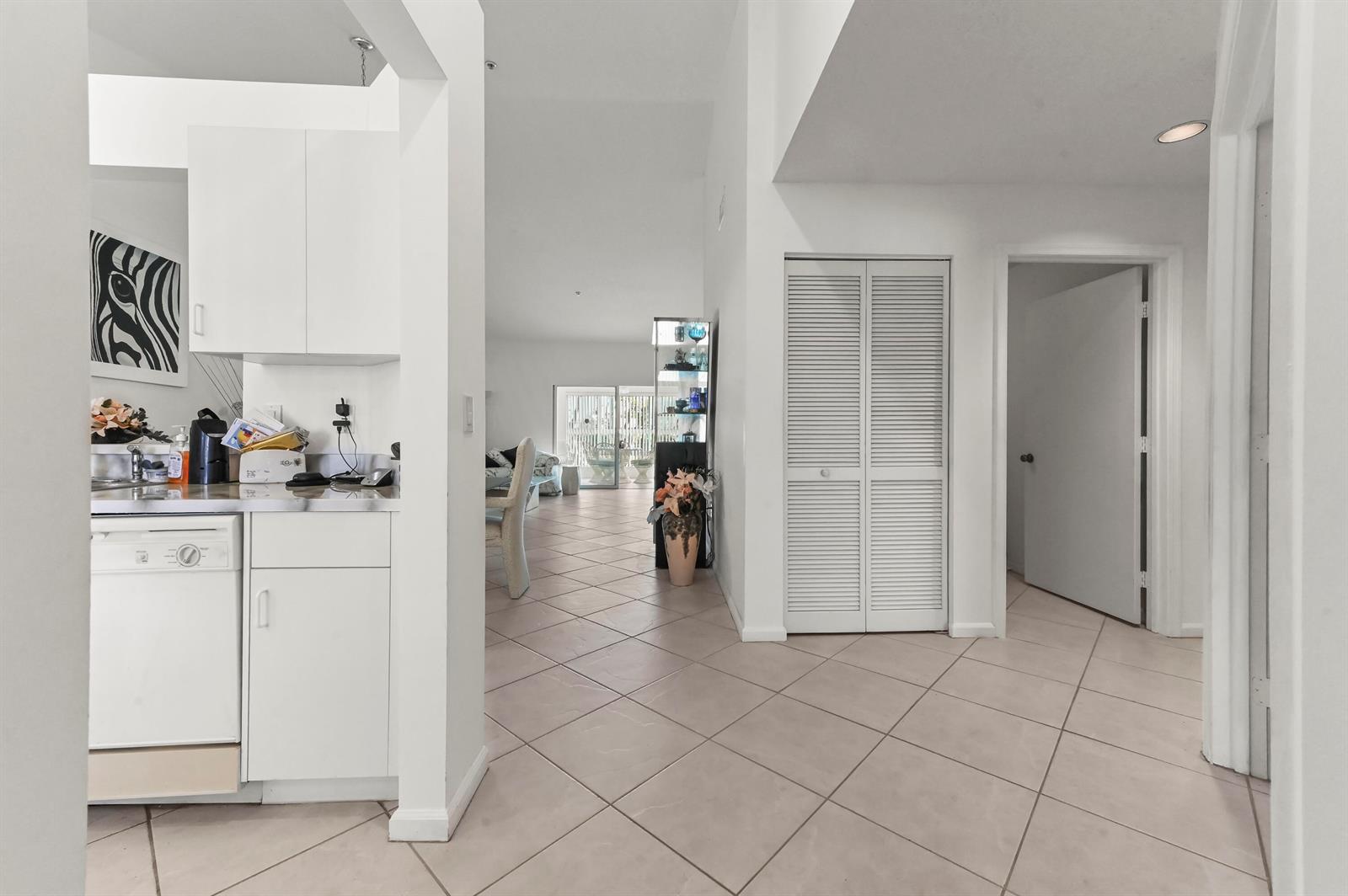 A kitchen with white cabinets opens into a tiled living area with a sliding glass door — 5952 Regal Glen Drive # 207, Boynton Beach FL 33437, BOYNTON BEACH, FL