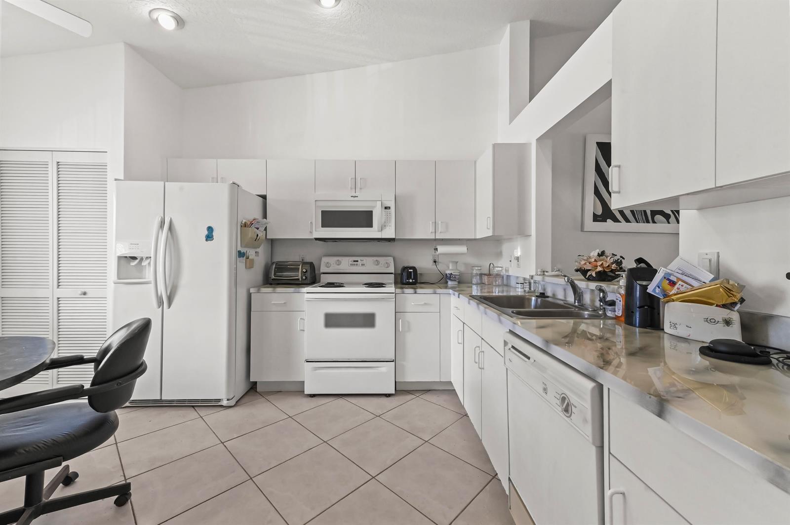 A kitchen features white cabinetry, white appliances, tile flooring, and a neutral countertop — 5952 Regal Glen Drive # 207, Boynton Beach FL 33437, BOYNTON BEACH, FL