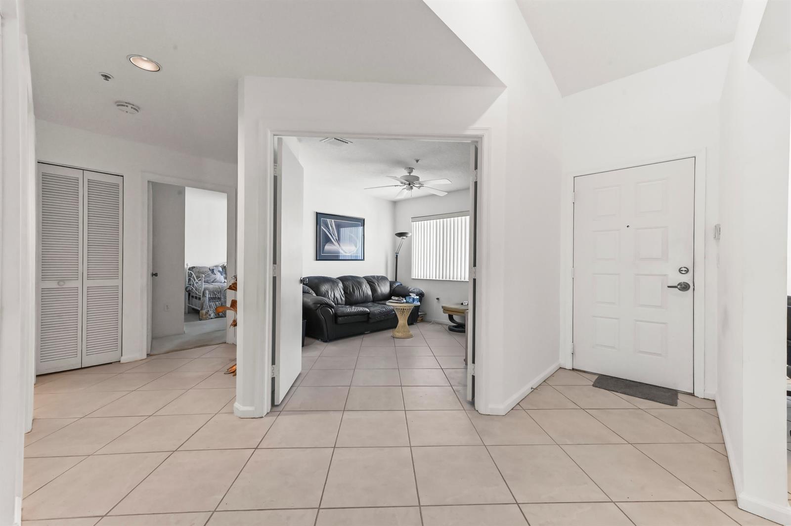An entryway with tiled floors leads to a living room with a black leather sofa — 5952 Regal Glen Drive # 207, Boynton Beach FL 33437, BOYNTON BEACH, FL