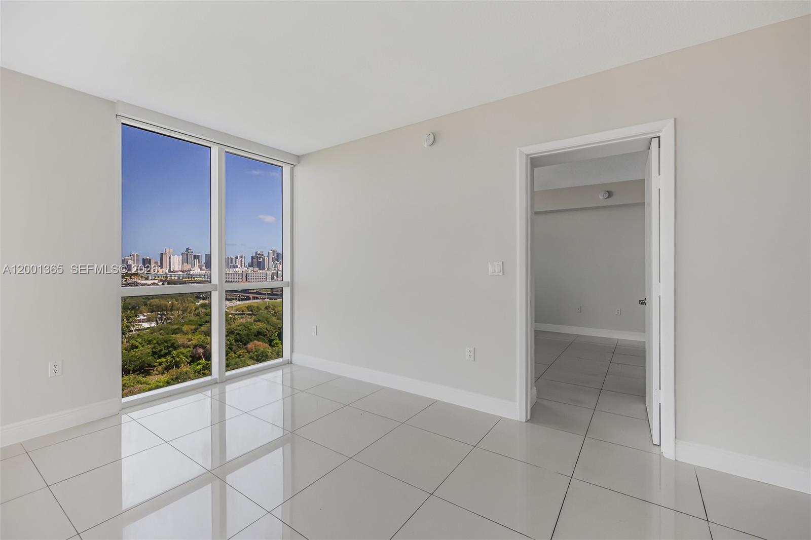 An empty room with white tile floors, large windows, and a doorway to another room — 1861 NW S River Dr # 2006, Miami FL 33125, MIAMI, FL