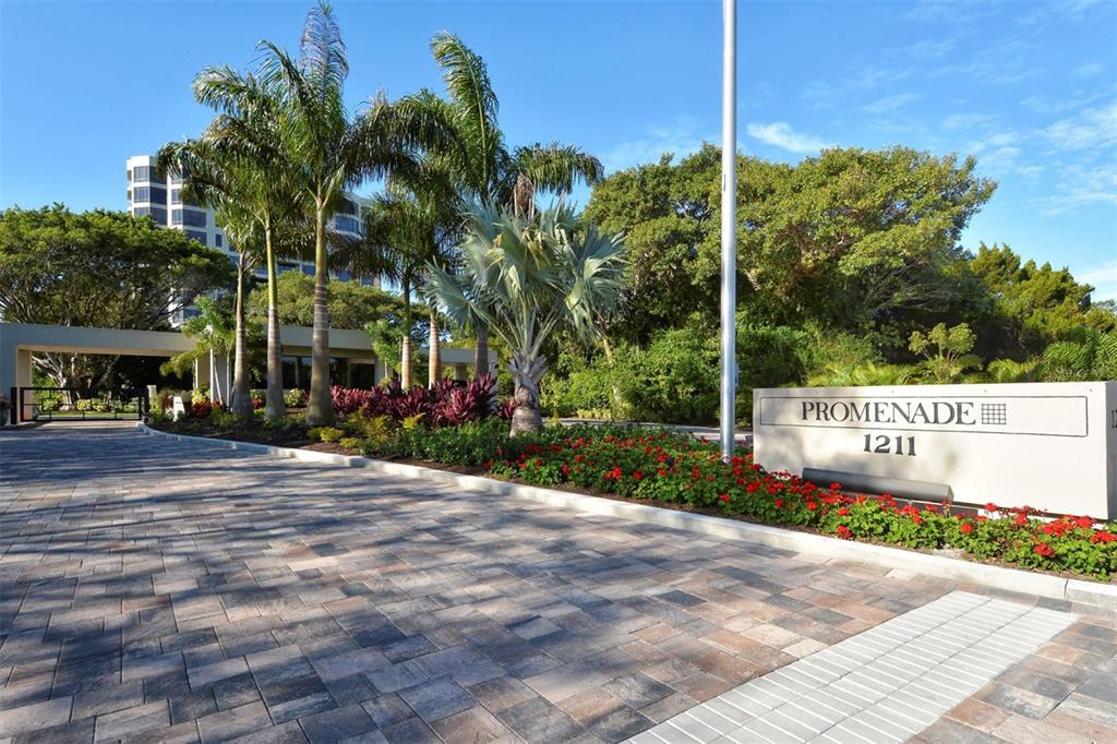 A paved driveway leads to a gated entrance with palm trees and a building sign — 1211 GULF OF MEXICO DRIVE UNIT 105, LONGBOAT KEY, FL