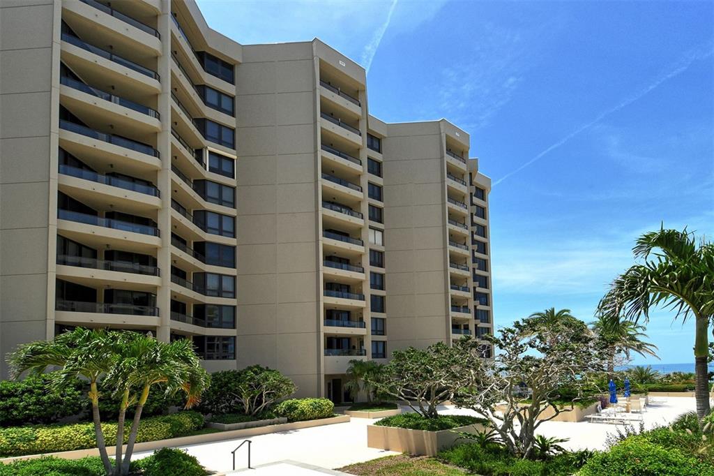 A multi-story beige condominium building with balconies overlooks a landscaped courtyard with palm trees — 1211 GULF OF MEXICO DRIVE UNIT 105, LONGBOAT KEY, FL
