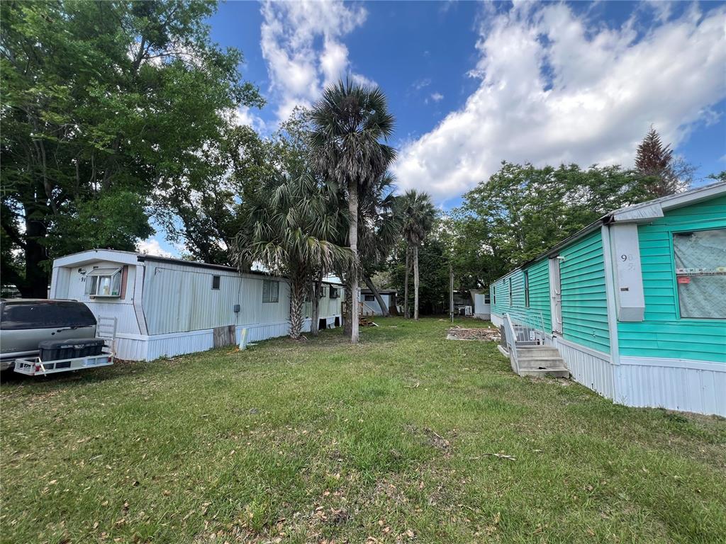 A grassy yard sits between two mobile homes under a blue sky with palm trees — 30 WAFFORD STREET, UMATILLA, FL