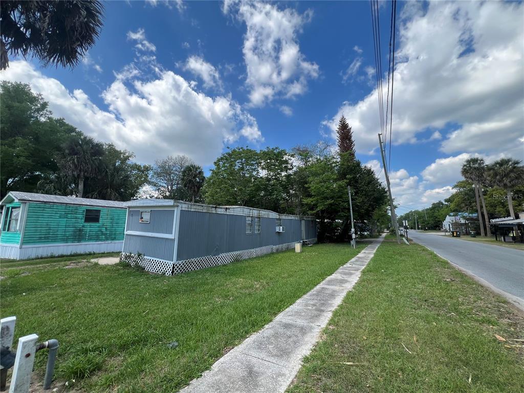 A gray mobile home sits next to a sidewalk along a road under a blue sky — 30 WAFFORD STREET, UMATILLA, FL