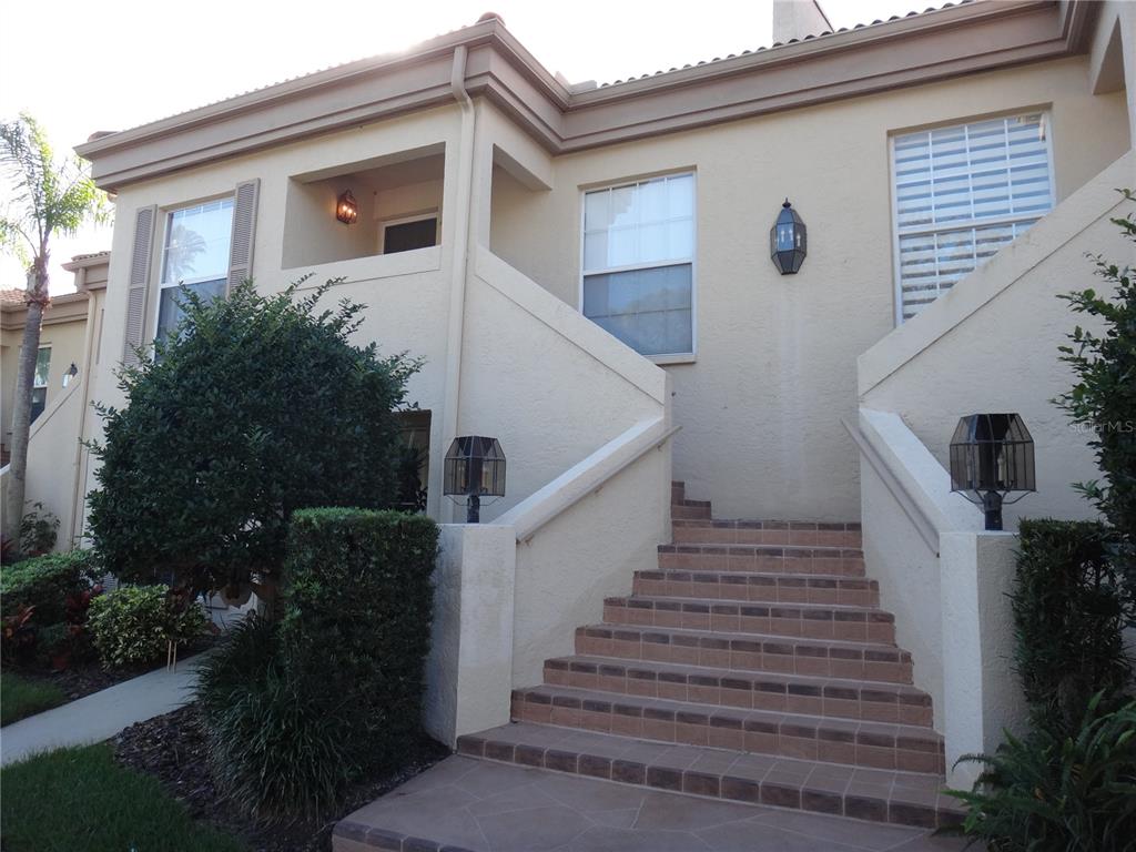 A set of tiled stairs leads to the entrance of a beige two-story residential building — 4493 LONGMEADOW UNIT 76, SARASOTA, FL