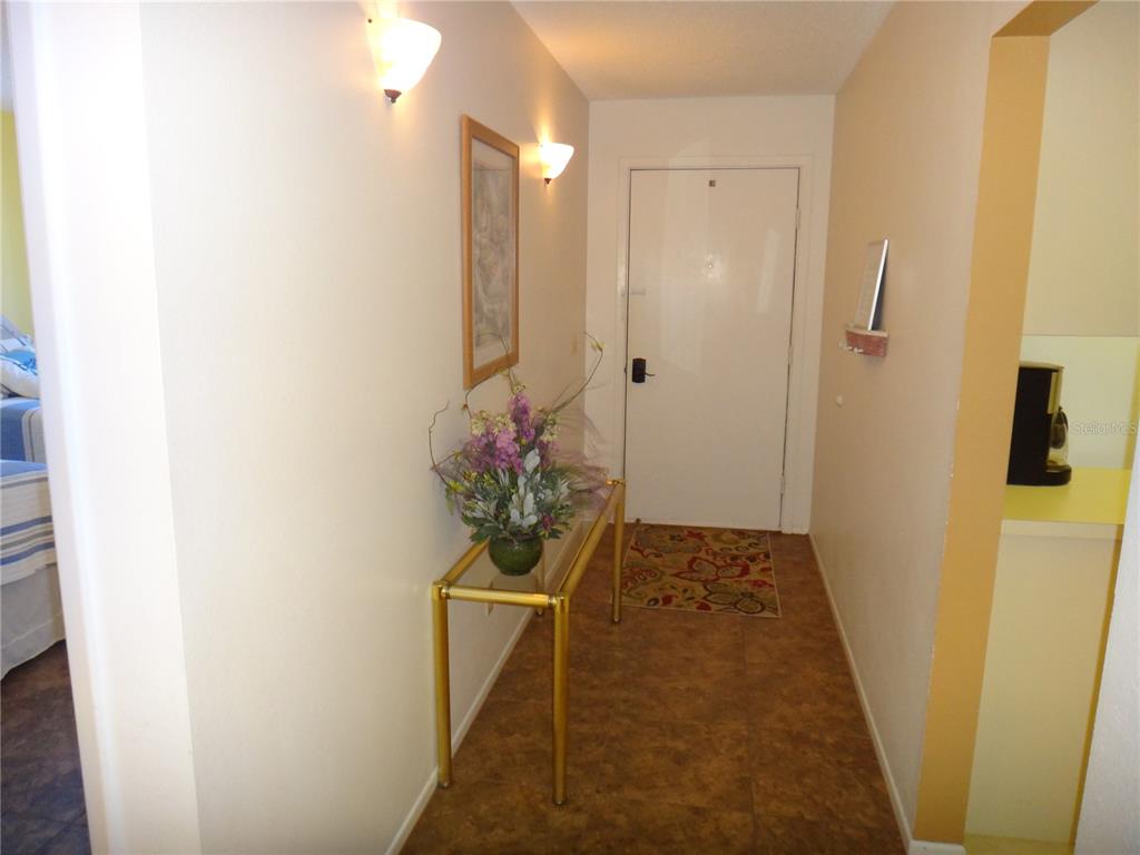 An entryway features a glass console table, floral arrangement, wall sconces, and a white door — 4493 LONGMEADOW UNIT 76, SARASOTA, FL