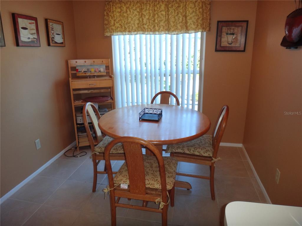 A dining area features a round wooden table, four chairs, and a window with blinds — 4493 LONGMEADOW UNIT 76, SARASOTA, FL