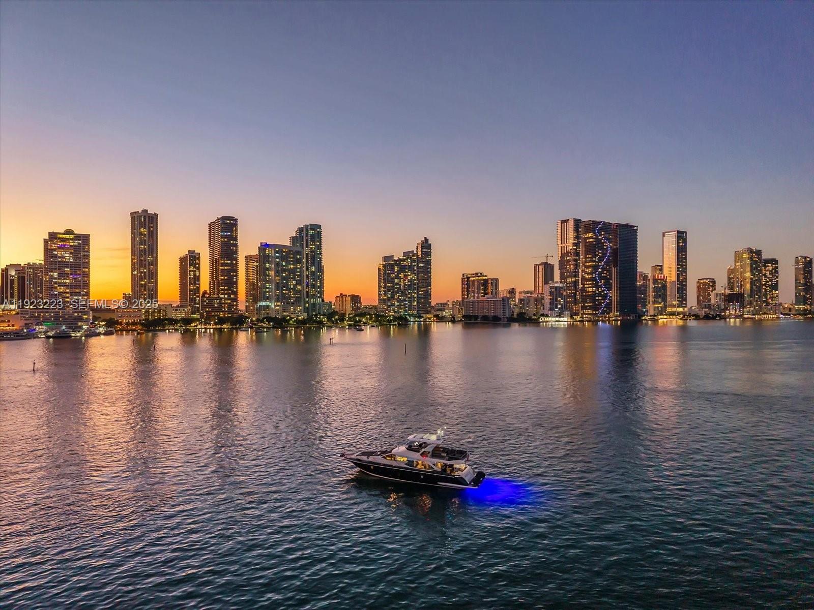 A yacht with blue underwater lights cruises on the water before a city skyline at sunset — 851 N Venetian Dr, Miami FL 33139, MIAMI, FL