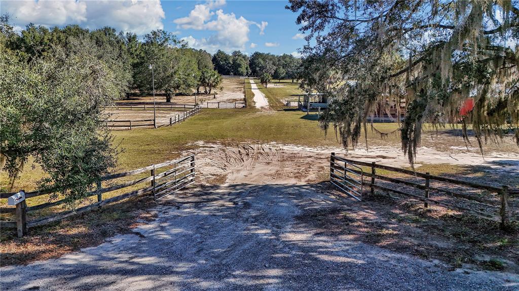A gravel driveway leads through an open gate into a grassy, fenced rural property — 11375 N CIRCLE M AVENUE, DUNNELLON, FL