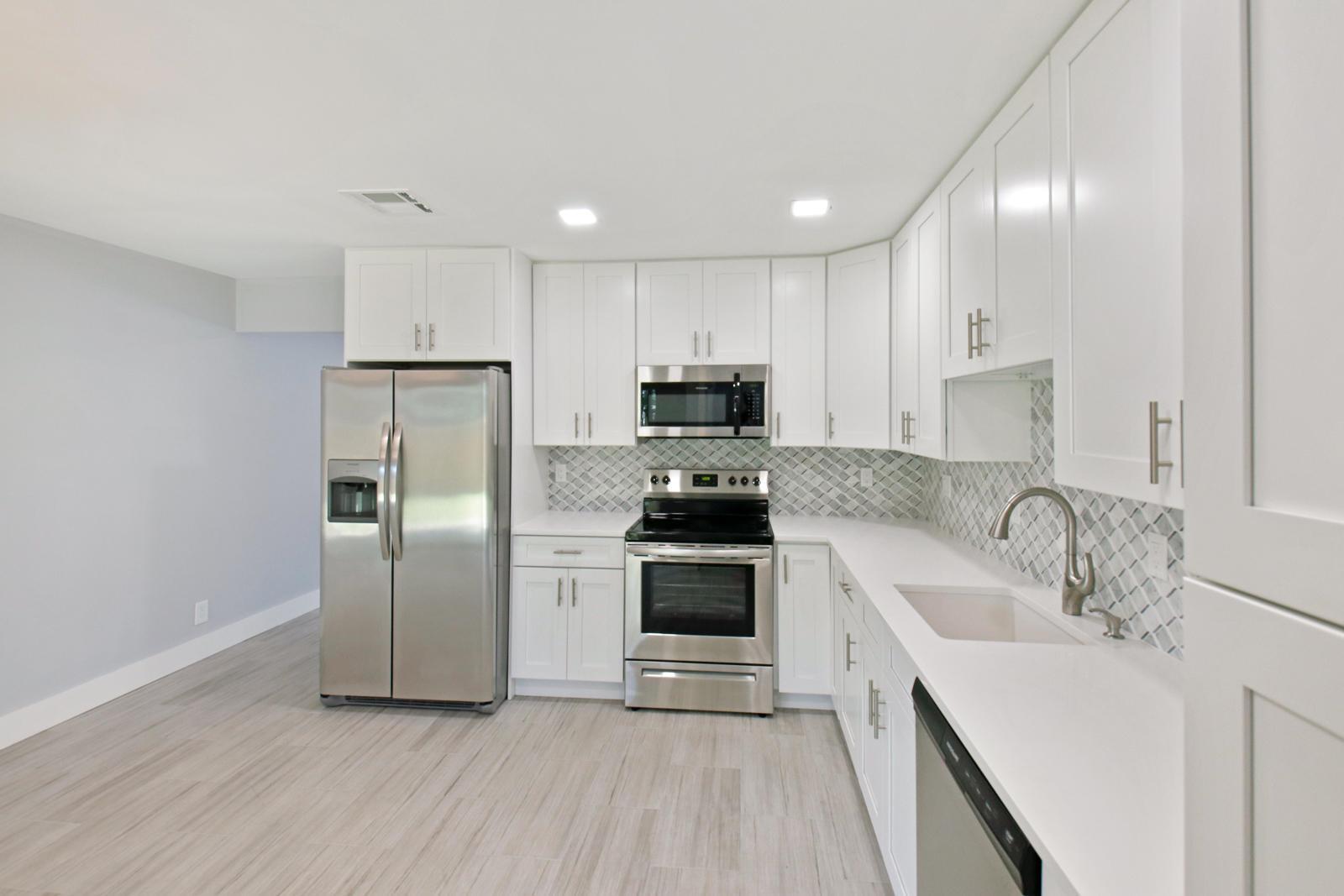 A modern kitchen features white cabinets, stainless steel appliances, and a light-colored tiled backsplash — 9128 Roan Lane, West Palm Beach FL 33403, WEST PALM BEACH, FL