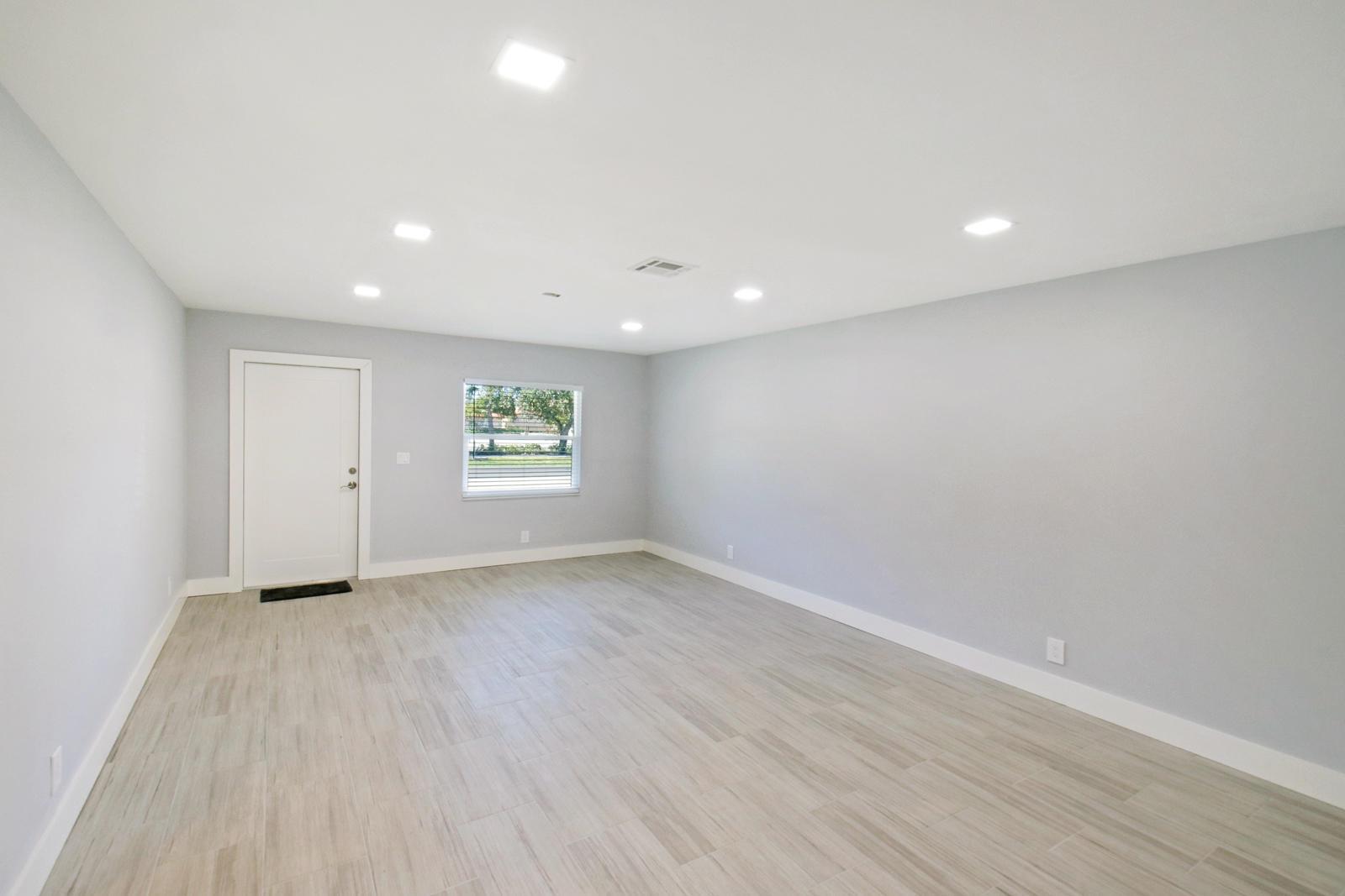 A bright, empty room features light gray walls, white trim, and wood-look tile flooring — 9128 Roan Lane, West Palm Beach FL 33403, WEST PALM BEACH, FL