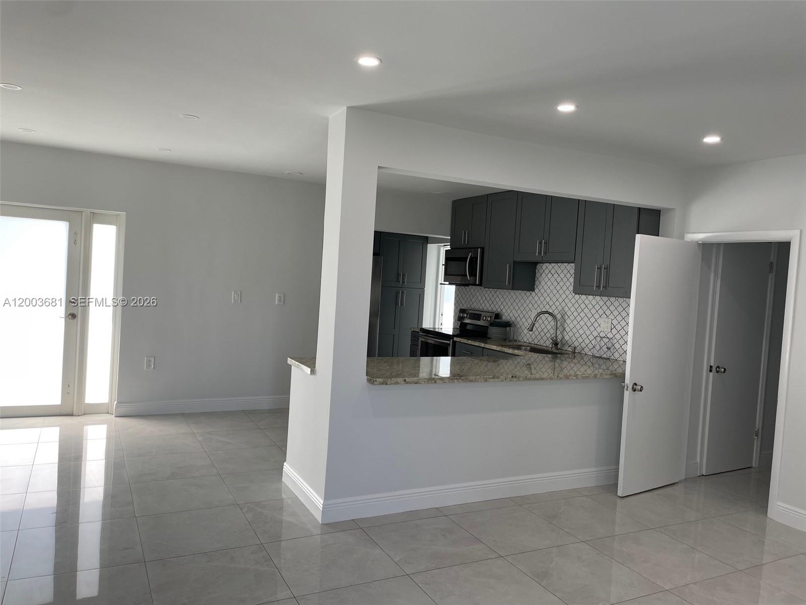 A kitchen with dark cabinets and a granite countertop overlooks an open-concept living area — 8640 SW 125th Ter, Miami FL 33156, MIAMI, FL