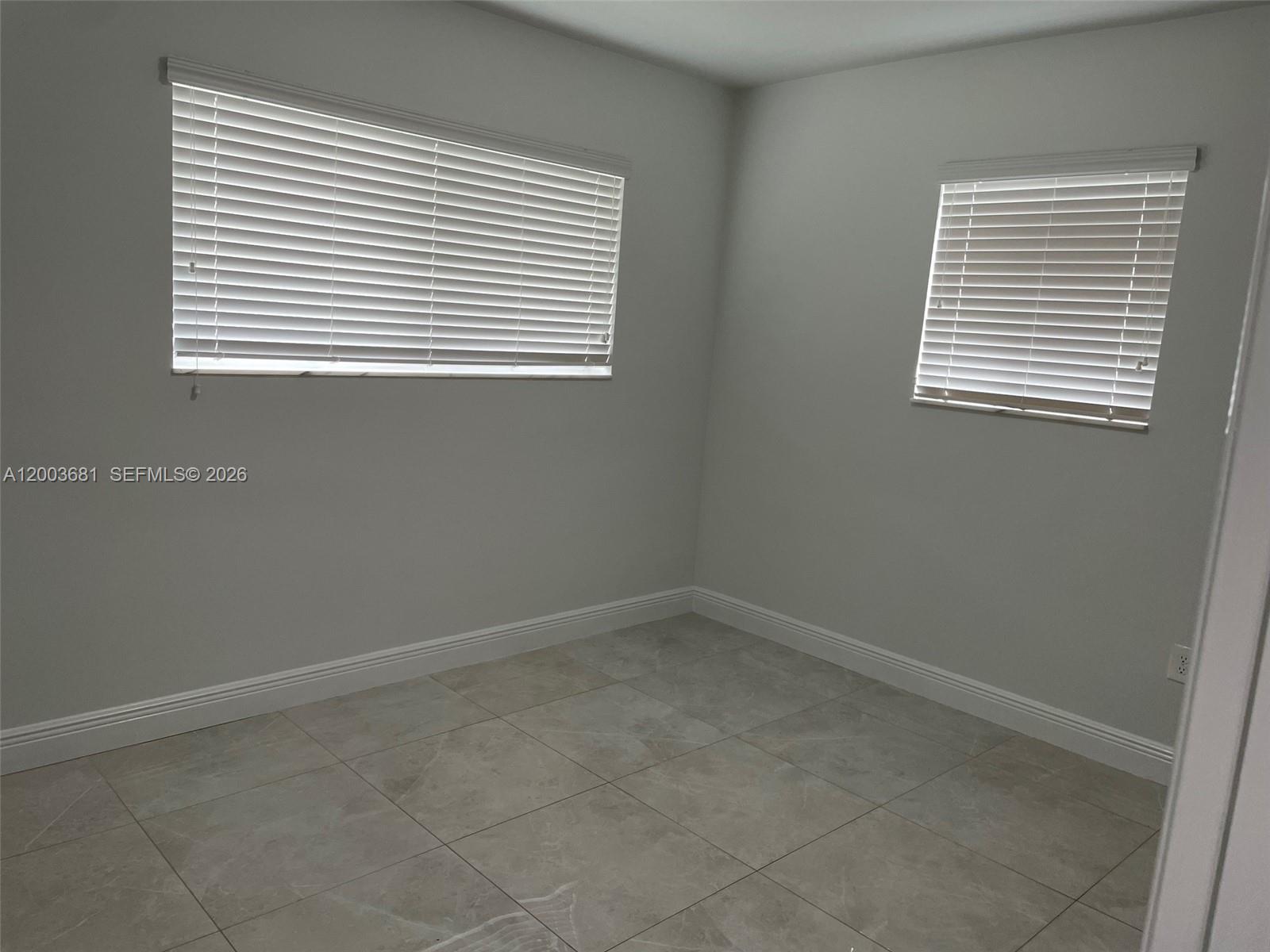 An empty room features light gray walls, large floor tiles, and two windows with blinds — 8640 SW 125th Ter, Miami FL 33156, MIAMI, FL