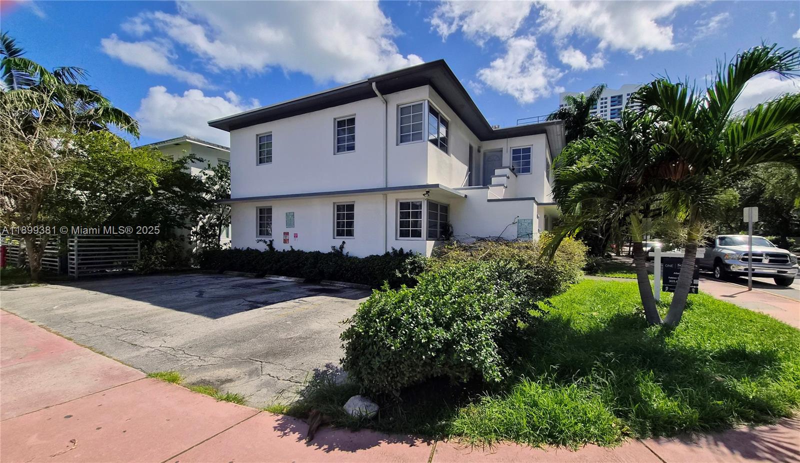 A two-story white building with a flat roof stands beside a paved parking area — 1485 Bay Rd, Miami Beach FL 33139, MIAMI BEACH, FL