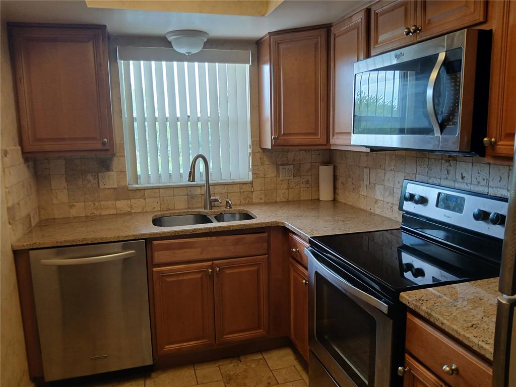 A kitchen features wood cabinets, granite countertops, stainless steel appliances, and a tiled backsplash — 5880 38TH AVENUE N UNIT 304, ST PETERSBURG, FL