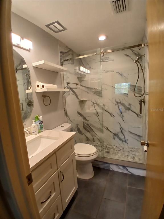 A bathroom featuring a white vanity, a toilet, and a glass-enclosed walk-in shower with marble-look tile — 5880 38TH AVENUE N UNIT 304, ST PETERSBURG, FL