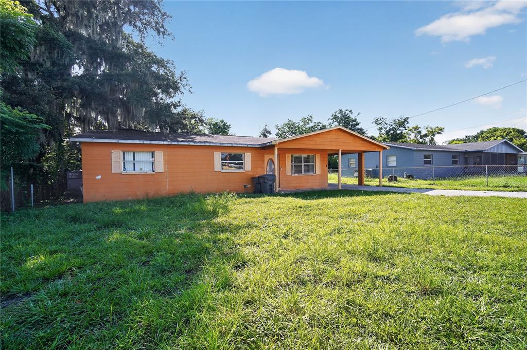 A single-story orange house with a front carport sits on a grassy lot — 1229 EL CAMINO ROAD, LAKELAND, FL