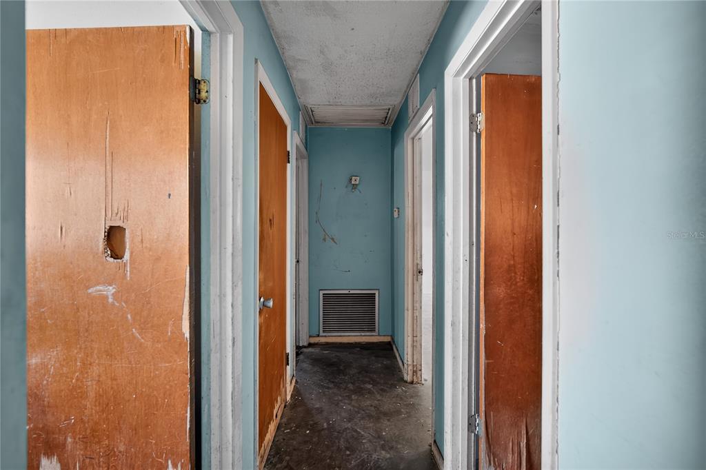 A narrow hallway with light blue walls, wood doors, and a dark, unfinished floor — 1229 EL CAMINO ROAD, LAKELAND, FL