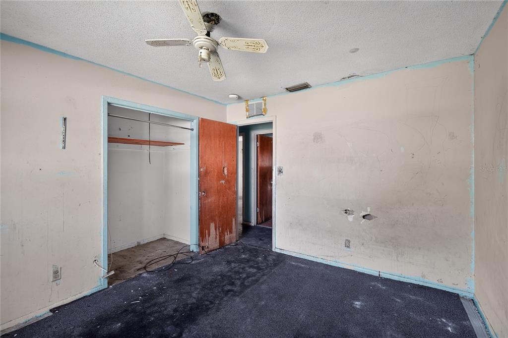 A bedroom with dark carpet, a ceiling fan, a closet, and damaged walls — 1229 EL CAMINO ROAD, LAKELAND, FL