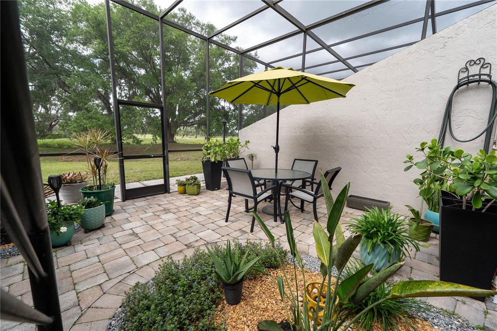 A screened-in patio features a paved floor, a dining set with an umbrella, and potted plants — 335 BOBBY JONES ROAD UNIT 335, SARASOTA, FL