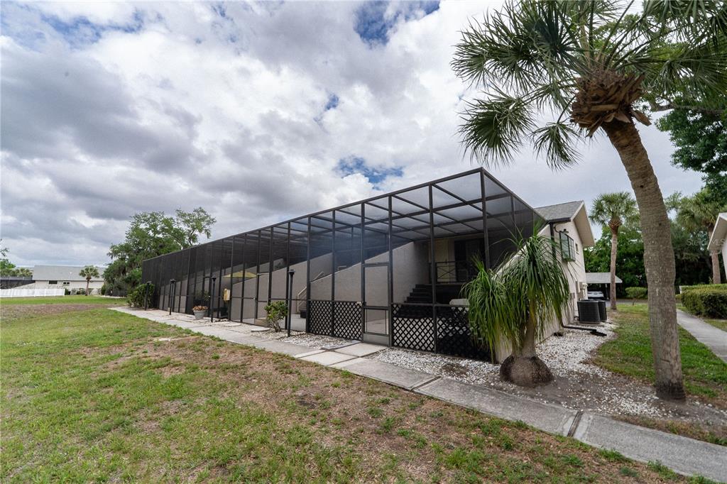 A large screened-in patio enclosure extends from the rear of a house with palm trees — 335 BOBBY JONES ROAD UNIT 335, SARASOTA, FL