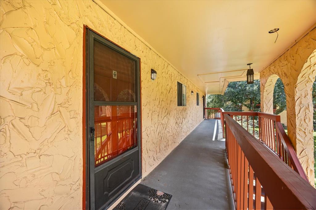 An outdoor covered walkway features textured yellow walls, a screen door, and a wooden railing — 2858 N POWERS DRIVE UNIT 123, ORLANDO, FL