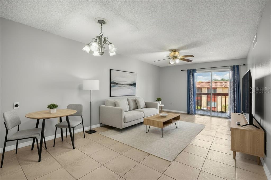 This virtually staged living room features tile flooring, a dining area, and a sliding glass door — 2858 N POWERS DRIVE UNIT 123, ORLANDO, FL