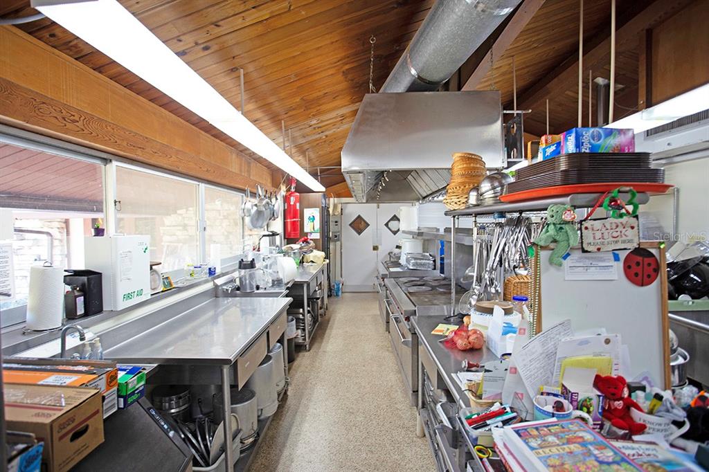 A commercial kitchen features stainless steel counters, a large ventilation hood, and wood-paneled ceilings — 3115 DRYER AVENUE, LARGO, FL