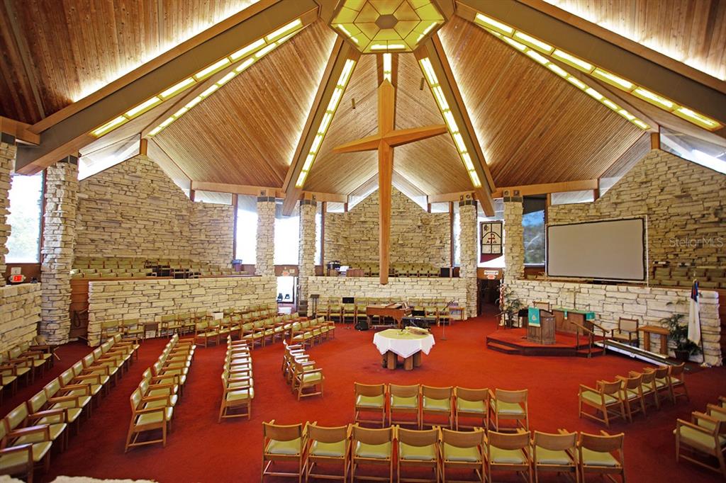 A church sanctuary features a high wood-paneled ceiling, stone walls, and rows of chairs — 3115 DRYER AVENUE, LARGO, FL