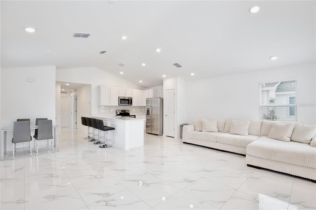 An open-concept living area features white marble-look tile floors, a white kitchen, and a sectional — 1709 TEAGAN LANE, WINTER HAVEN, FL