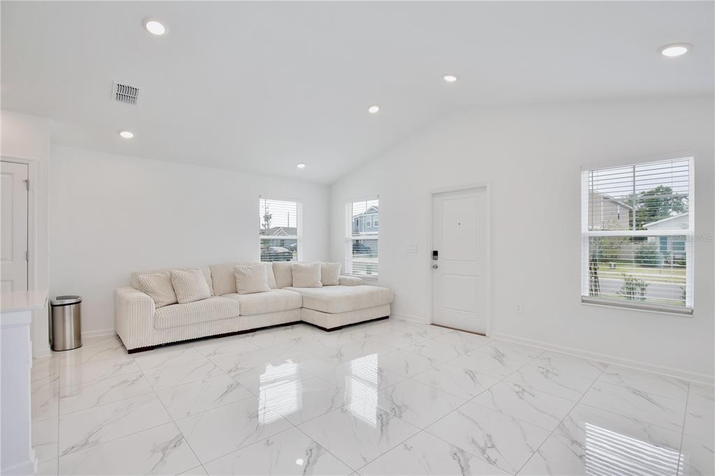A bright living room features white walls, marble-look tile flooring, and a large sectional sofa — 1709 TEAGAN LANE, WINTER HAVEN, FL