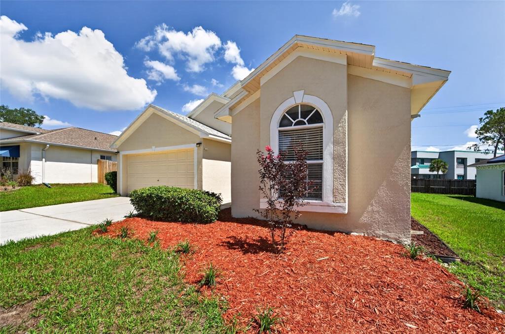 A tan single-story house with a two-car garage, arched window, and red mulch landscaping — 418 HENDERSON AVENUE, SEFFNER, FL