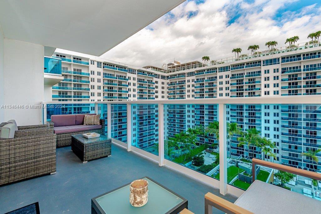 A balcony with outdoor furniture overlooks a large residential building with glass railings — 2301 Collins Ave # 1115, Miami Beach FL 33139, MIAMI BEACH, FL