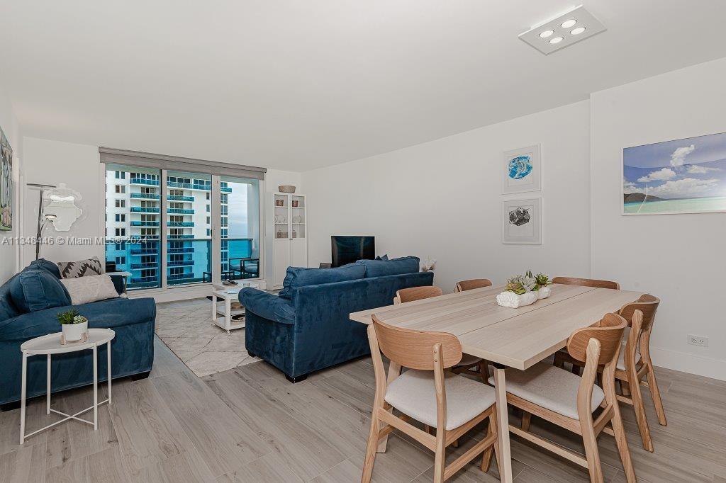 A living and dining area features blue sofas, a light wood table, and balcony views — 2301 Collins Ave # 1115, Miami Beach FL 33139, MIAMI BEACH, FL