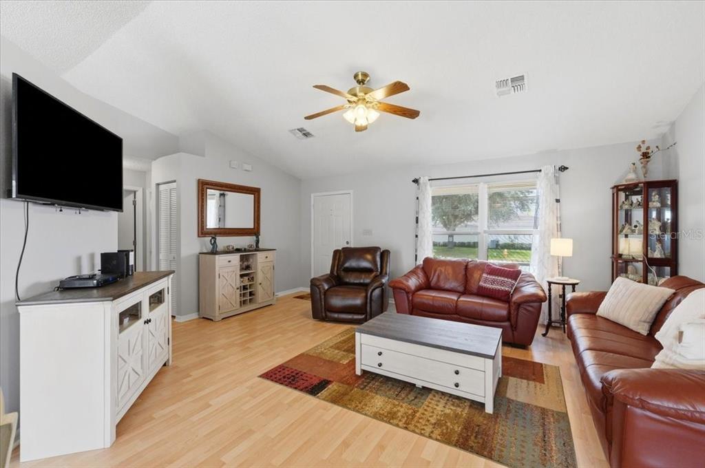 A living room features light wood flooring, a ceiling fan, and brown leather furniture — 1001 CANARY CIRCLE S, LAKELAND, FL