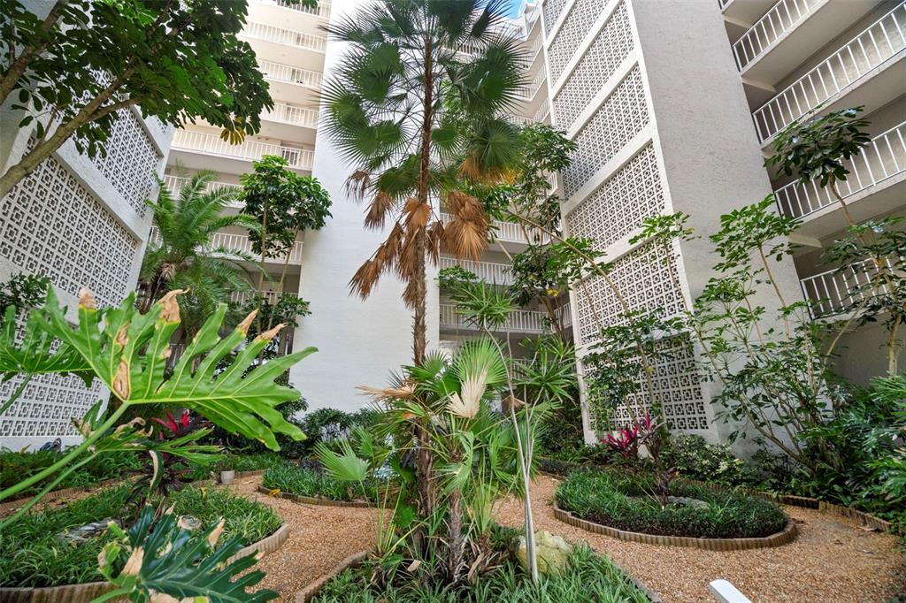 A central courtyard features a tall palm tree, lush tropical plants, and white lattice walls — 500 N OSCEOLA AVENUE UNIT 406, CLEARWATER, FL