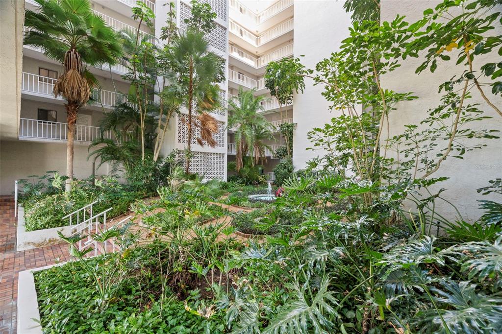 An interior courtyard with lush tropical plants, palm trees, and a small fountain — 500 N OSCEOLA AVENUE UNIT 406, CLEARWATER, FL