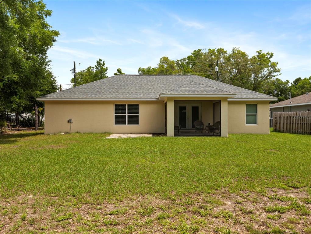 The rear exterior of a single-story house features a screened-in porch and a grassy yard — 9432 SE 152ND PLACE, SUMMERFIELD, FL